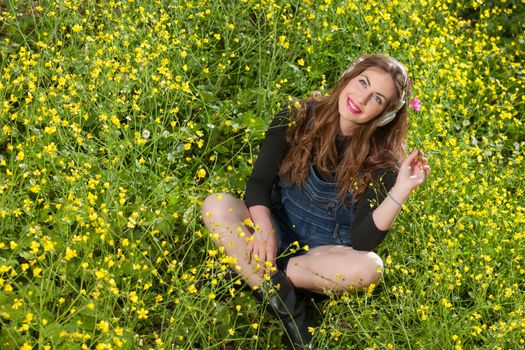 portrait of a beautiful young girl with headphones among yellow flowers of a garden