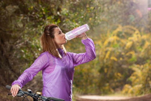 Beautiful fit young girl with bicycle drinking water in the nature