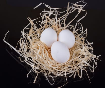 Three chicken eggs in the nest like On a black background