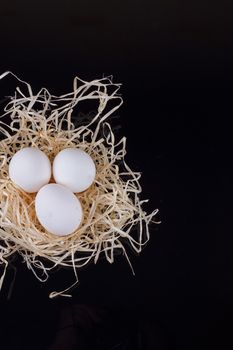 Three chicken eggs in the nest like On a black background