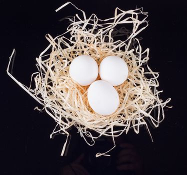 Three chicken eggs in the nest like On a black background