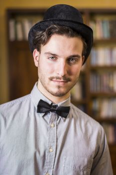 Attractive young man wearing top hat and bow tie, looking at camera. Indoors shot