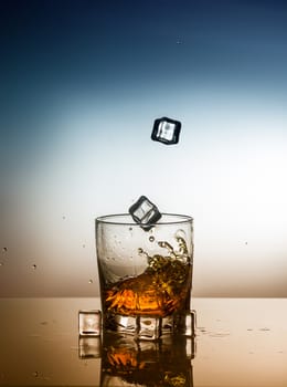 a glass of whiskey with falling ice cubes