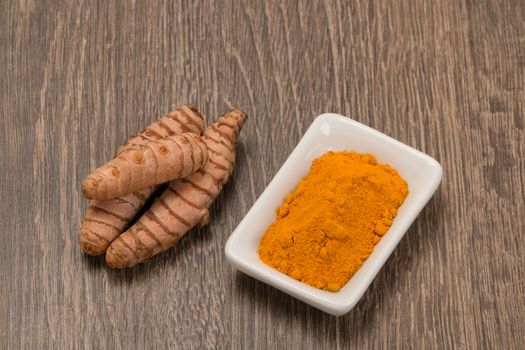 Turmeric powder with turmeric root over wood background