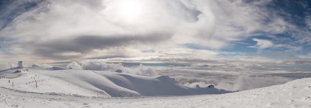 The top of the mountain Helmos in Kalavrita ski resort with snow and clouds in a sunny day