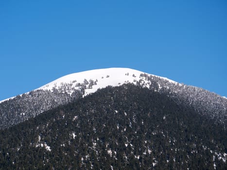 The top of the mountain Helmos in Kalavrita ski resort with snow and clouds in a sunny day