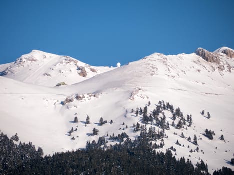 The top of the mountain Helmos in Kalavrita ski resort with snow and clouds in a sunny day