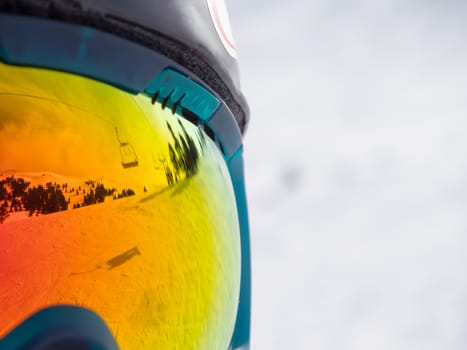 close up of colorfull googles that reflecting the landscape of a ski resort with lift 
