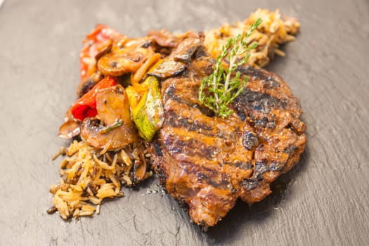 Grilled steak served with rice and vegetables on a graphite plate