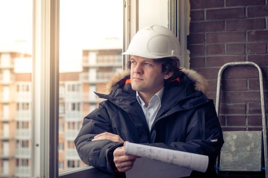 Pensive young man builder in hard hat standng and thinking. Soft focus, toned