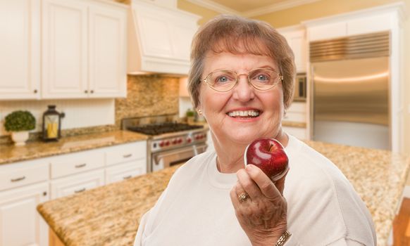 Happy Senior Adult Woman with Red Apple Inside Kitchen.