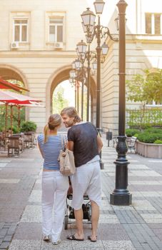 Romantic young happy couple kissing and pushing a stroller outside.