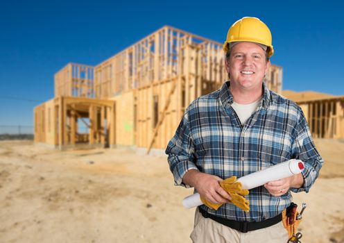 Contractor with Plans and Hard Hat In Front of New House Framing at Construction Site.