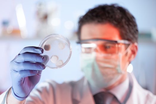 Mask and goggles protected life science researcher observing potentially infectious cells in petri dish. Focus on scientist's eye. Healthcare and biotechnology concept.