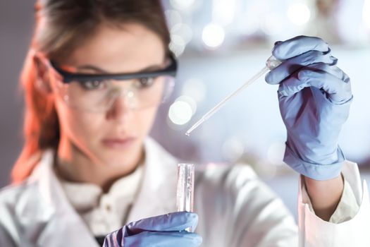 Life scientists researching in laboratory. Focused female life science professional pipetting solution into the glass cuvette. Lens focus on researcher's eyes. Healthcare and biotechnology concept.