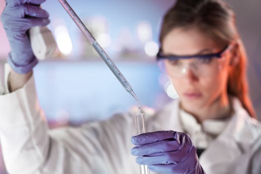 Life scientists researching in laboratory. Focused female life science professional pipetting solution into the glass cuvette. Lens focus on researcher's eyes. Healthcare and biotechnology concept.