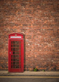 Traditional Red British Telephone Box Against A Red Brick Wall With Copy Space