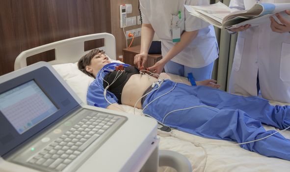 A nurse is fixing cardiograph sensors on a young female patient in modern hospital.