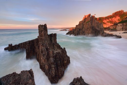 Ocean flows around volcanic sea stacks as first light strikes the landscape