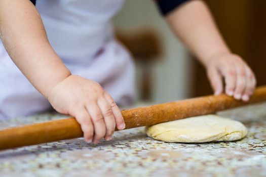 Hands baking dough with rolling pin on table. little chef  bake in kitchen.