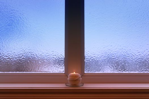 Frosted window, and ball of yarn candle on a windowsill.