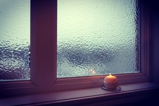 Candle burning near a frosted window in twilight. Winter evening.