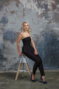 girl in a black dress with long flowing hair sitting on a high chair next to a wall