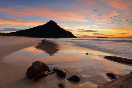 Zenith Beach and reflections in the shorebreak   Mt Tomaree  and Boondelbah island in silhouette against the beautiful  dawn sunrise light illuminating the sky