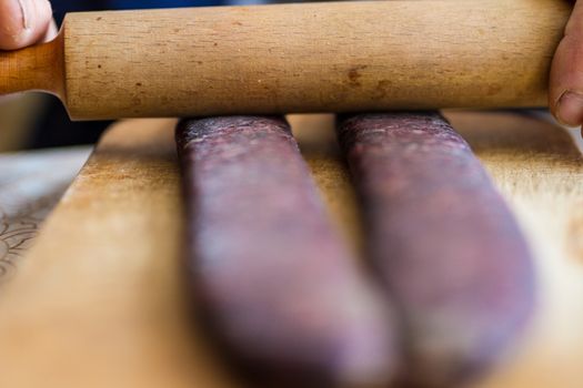 Closeup of man hands rolling over homemade sausages to make them flat for drying