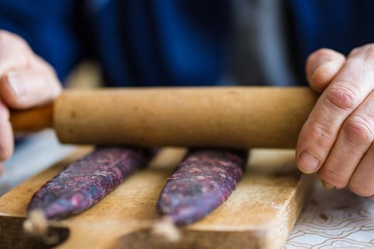 Closeup of man hands rolling over homemade sausages to make them flat for drying