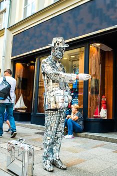 a man in a mirror suit with a suitcase and a bicycle is calling to the Krakow store