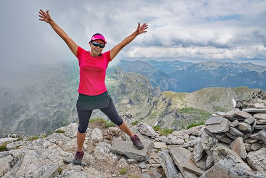 A beautiful woman is spreading her hands on a mountain peak.