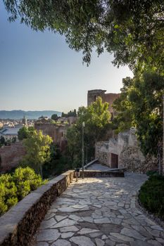 Stone pathway leading down the hill overlooking Malaga, Spain, Europe with trees on either side on a bright summer day