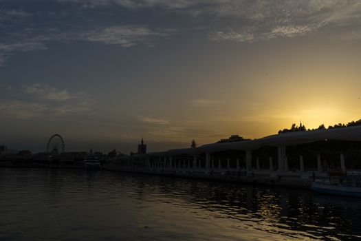 Giantwheel and the docking harbour of Malaga with sun set in the background in Malaga, Spain, Europe at the golden hour