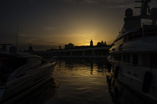 Golden sun sets behind the cathedral viewed between two boats at Malaga, Spain, Europe during golden hour