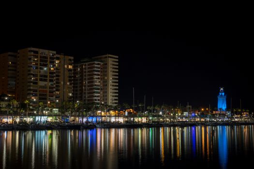 View of Malaga city and lighthouse and their reflections on water from harbour, Malaga, spain, Europe at night with illuminations