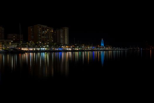 View of Malaga city and lighthouse and their reflections on water from harbour, Malaga, spain, Europe at night with illuminations