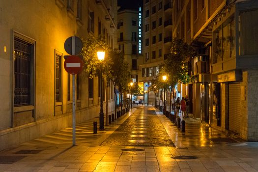 Cobblestone street lit with yellow street lamps at night in Malaga, Spain, Europe