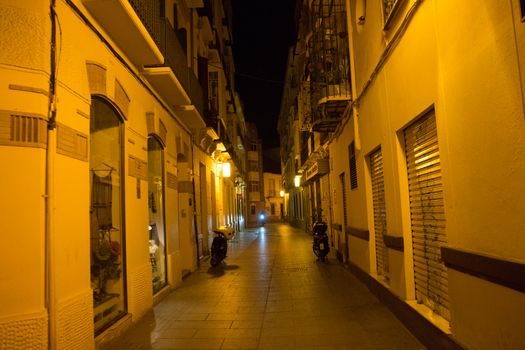 Cobblestone street lit with yellow street lamps at night in Malaga, Spain, Europe