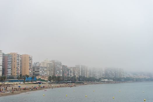 The building along the coastline at Malagueta beach covered by fog in Malaga, Spain, Europe on a foggy morning