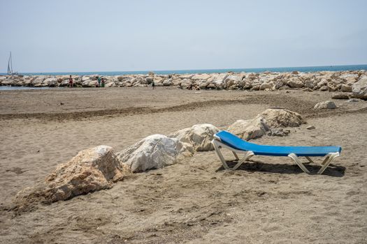 Sunbed on the rocky beack at Malagueta in Malaga, Spain, Europe on a cloudy morning with the ocean and boat in the ground