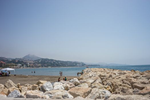 View of the ocean at Malagueta beach with rocks at Malaga, Spain, Europe on a clear sky morning with a hill in the background