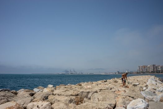 A father helping his son walk on the rocks on the Malagueta beach in Malaga, Spain, Europe with a clear ky in the morning