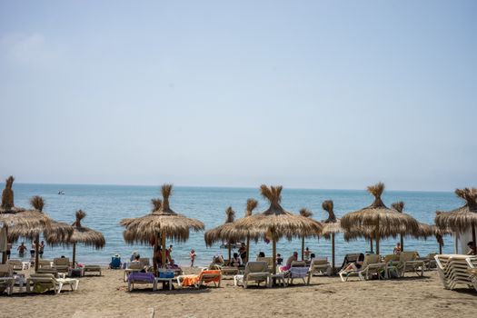 Holiday scene at the malagueta beach with palm roofs on a summer day with the ocean in the background in Malaga, Spain, Europe with clear skies