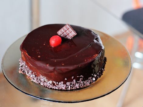 Delicious chocolate cake with cherries in a plate on a glass table.