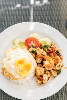 Spicy fried seafood with basil leaves on jasmine rice and fried egg