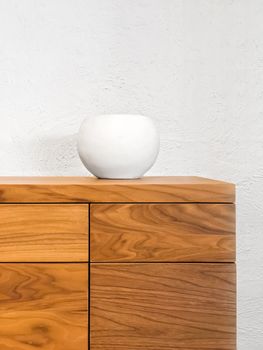 Simple white ceramic vase decorating a wooden chest of drawers.