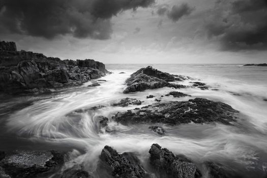 Seascape at low tide with moody clouds and pending storms and swirling ocean currents around the exposed rocks.