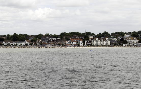 people on the beach with the houses of the german city Kiel as background