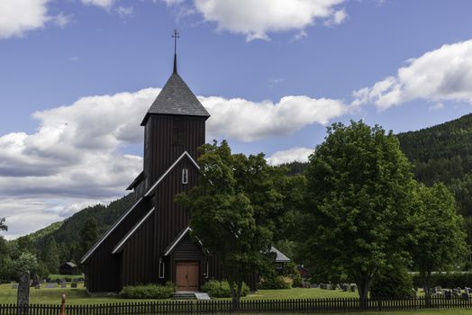 brown  wooden stave church near Leira in Norway with cemetery